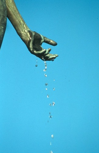 Standing: detail view of bronze figure's left hand dripping water