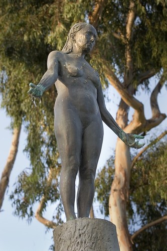 Standing: detail of figure on top of column with water falling from hands and eucalpytus trees in the background