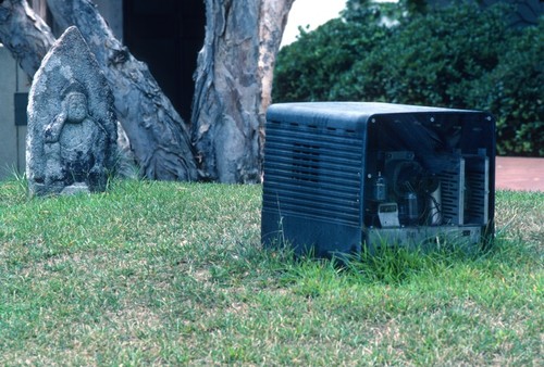 Something Pacific: detail: carved stone buddha contemplating old television set with inner workings of tv exposed