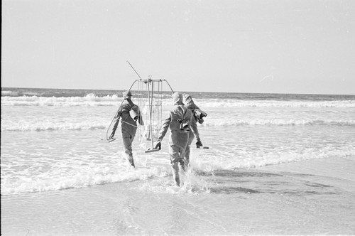 A early suspended sediment trap being taking into the ocean by some Scripps Institution of Oceanography staff. Photo includes two unidentified men and Robert Lester Wisner (man in center). Note the early "water suits" being used which were gathered and tied at their backs. This was before neoprene wet-suits, as we know them today. Circa 1948