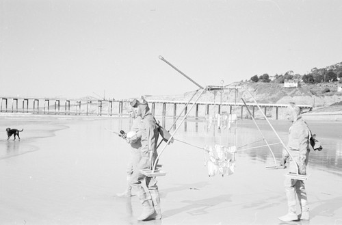 A early suspended sediment trap being taking into the ocean by some Scripps Institution of Oceanography staff, near the institutions pier. Photo includes two unidentified men and Robert Lester Wisner (man on far right). Note the early "water suits" being used which were gathered and tied at their backs. This was before neoprene wet-suits, as we know them today. Circa 1948