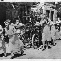 Group of women including Geraldine McConnell, in 1940s dress pulling an antique firefighting pumper