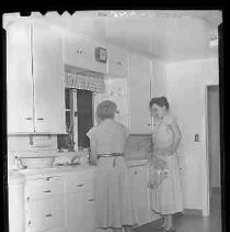 Two women standing next to a kithchen sink