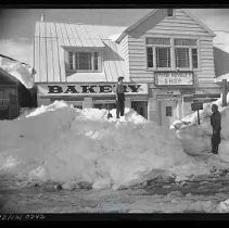 Sierra snowstorm - Two people on piles of snow in front of bakery building