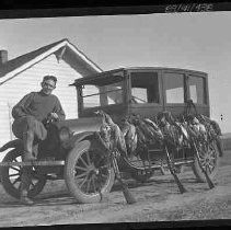 Man with dead geese next to an automobile