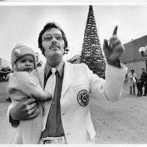 Stan Kline, the conductor of the Catholic School Band, leading the band in Christmas Carols on the K Street Mall as he holds his 9-month old son, Nathan