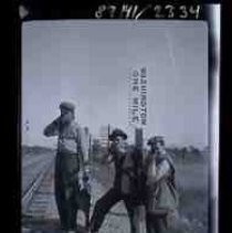 Three men standing by railroad tracks pointing guns