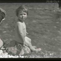 Naked baby sitting on a rock in water