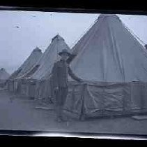 An unidentified man standing next to a tent in a military encampment