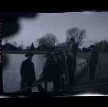 A group of nine men standing next to a fence along side a lake