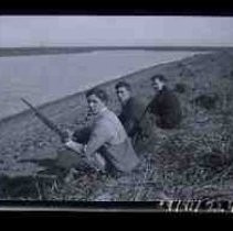 Three young men sitting at the edge of a wetland lake