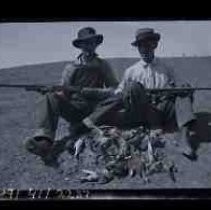 Two young men sitting in a field with a pile of dead doves