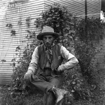 View of Henry Ellis of Orangevale seated on a stool in front of a building