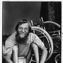 Gene Howard, a wheelchair athlete who competed in marathons, played tennis, and taught sports to handicapped children. He is shown sitting on grass next to wheelchair