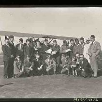 A group of men and two women standing next to a bi-plane