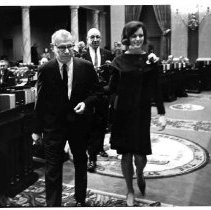 View of State Senator Al Rodda escorting the Camellia Queen, Joan Martin of Sacramento State College into the California Senate Chamber where she presented Senate Speaker pro-tem Hugh Burns with a potted camellia plant