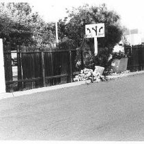 Broken fence with brick pillars, large pile of trash and street sign