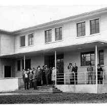 Unidentified building with people in business attire standing in front, and a water tower in background