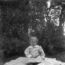 View of a child sitting on a blanket in a wooded area