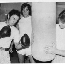 Joe Guevara punching the heavy bag as Tim Miller (right) and Jim Burchett look on