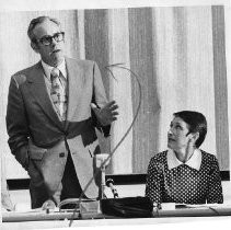 Richard (Dick) Desmond (attorney), who represents protestors speaks to a group in a cafeteria. On the right is Barbara E. Kelley, moderator
