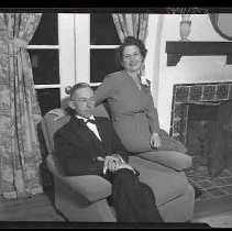 Unidentified man and woman sitting next to a fireplace
