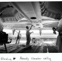 Workers, standing on a scaffolding platform, apply glazing to the State Assembly Chamber's ceiling as part of the California State Capitol restoration project
