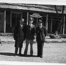 Photograph of Neasham standing in front of a "Billy the Kid Curio Shop" with two unidentified men, one in a military uniform