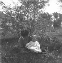View of a woman and child sitting on a blanket in the grass
