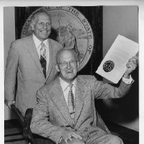 Goodwin Knight, Governor of California from 1953-1959. Here, he wheels another gentleman in a wheelbarrow in front of Great Seal of California