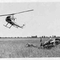 California Highway Patrol helicopter hovering over man lying next to crashed motorcycle in a field