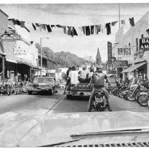 Caption reads: "Motorcyclists line both sides of California 49 in Angel's Camp during weekend frog jump festivities. Cyclists caused much concern as they parked 'bikes' 10 to 30 deep in places along the street" in Calaveras County