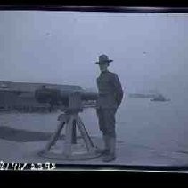 An unidentified soldier standing next to a canon placed on a dock