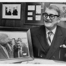 George E. Johnson, Sacramento businessman and restaurateur, shown with a photograph of himself taken with John F. Kennedy, and a photo with Lyndon B. Johnson in the background. Caption: "community leader" (Eppie Johnson was his son.)