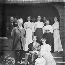 Exterior view of twelve people standing and sitting on the steps of a house