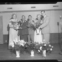 Three men and two women on a stage with flowers