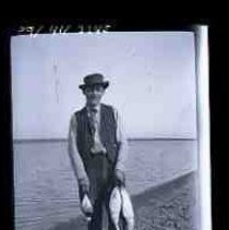 A young men standing on the bank of a wetland lake holding three water birds