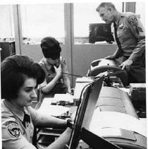 Caption reads: "Sergeant Ray Mayhugh, operations officer of the new highway partrol auto theft project watches as Carolyn Allman, foreground and Donna Prosser operate the new equipment."