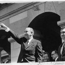 President Lyndon B. Johnson, on a campaign visit to Sacramento, smiles and gestures toward someone in crowd. Next to him, from left, are Assembly Speaker Jesse Unruh, Governor Pat Brown, and Senator Pierre Salinger