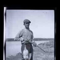 A young men sitting holding a shotgun and a dead duck