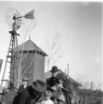 Unknown family outdoors in front of a tank house and windmill