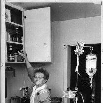 Carole Hoisington with a stand holding a pump and a solution bottle; she can pull it around the house, either plugged into an outlet or running on self-contained batteries. She mixes her own meds to treat her illness