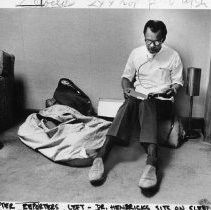 Dr. William Hendricks, who had talked to reporters in the Governor's Office, sits on his sleeping bag and reads a book from his duffel bag