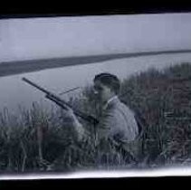 A young men sitting in cattails holding a shotgun