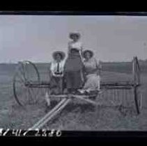 Three young women sitting on a horse drawn hay rake