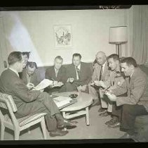 Eight men seated around a coffee table