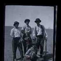 Four young men standing in a field holding bunces of dead doves