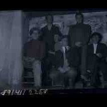 Six young men standing and sitting in a small room or shack