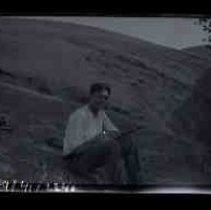 A young men sitting in an open grassland with a shotgun