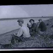 Three young men sitting at the edge of a lake